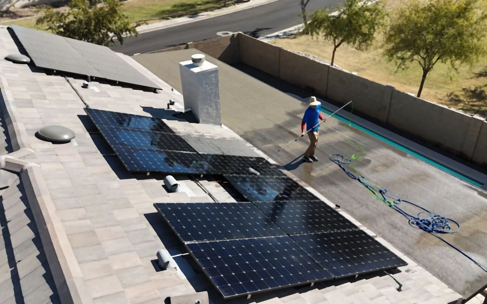 Drone view of a SunGuys technician cleaning rooftop solar panels with a water-fed pole