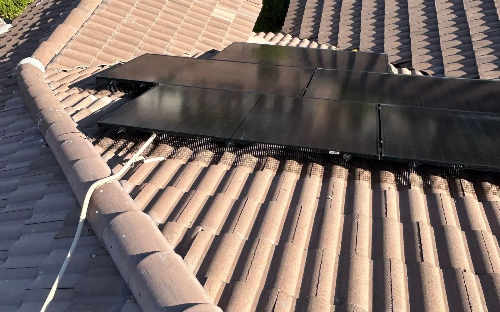 Close-up of black critter-guard mesh fitted along the edge of a solar array on a tile roof
