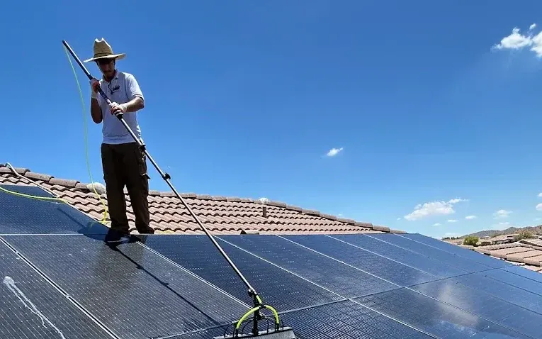 A SunGuys technician cleaning rooftop solar panels with a long-handled soft brush